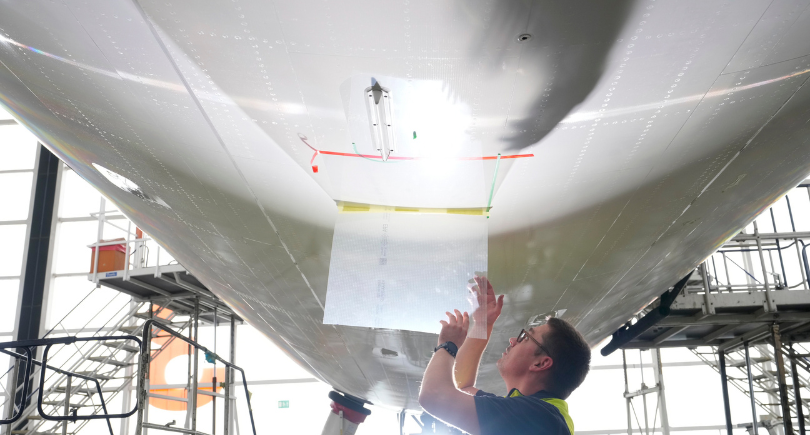 Technician applies AeroSHARK riblet film to an aircraft fuselage to improve aerodynamics and reduce fuel consumption.