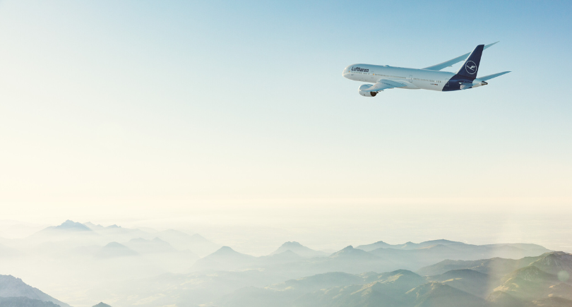 Lufthansa aircraft flies above mist-covered mountains, reflecting the airline’s focus on sustainable aviation initiatives.