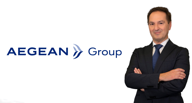 AEGEAN Group CEO Michalis Kouveliotis poses in a suit beside the company logo.