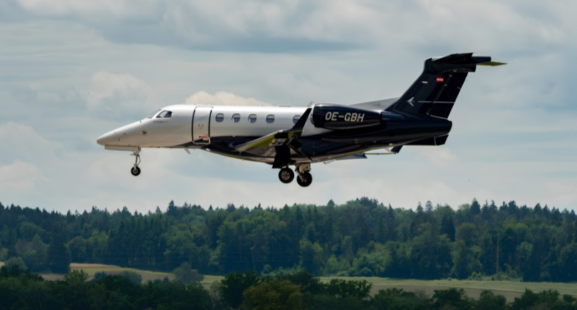 Embraer Phenom 300 business jet flying above a forested landscape during flight.