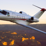 Cessna Citation CJ4 business jet flying over a canyon at sunset.