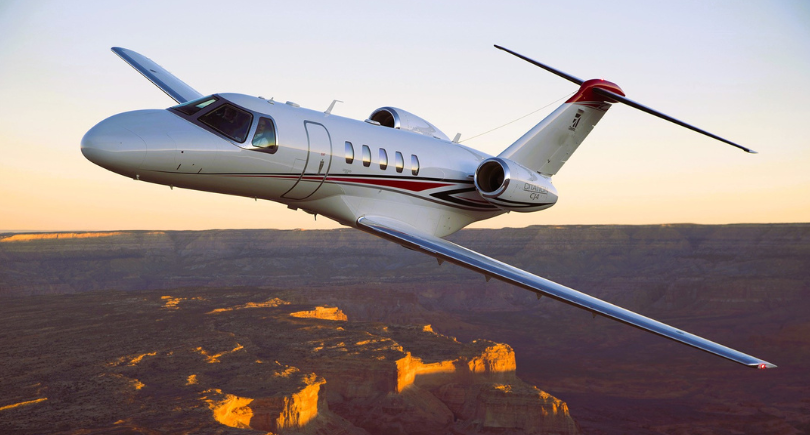 Cessna Citation CJ4 business jet flying over a canyon at sunset.